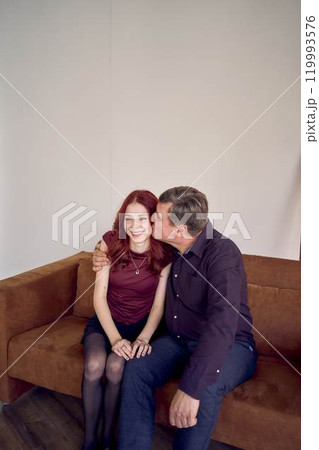 middle-aged father and teenage daughter together on sofa middle-aged father and teenage daughter together on sofa 119993576