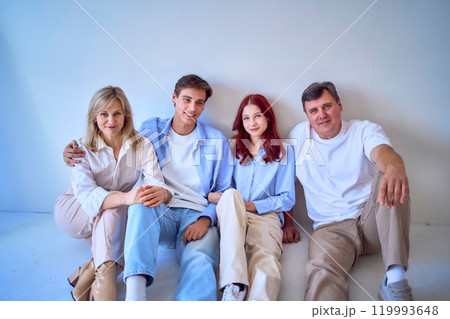 a family, middle-aged husband and wife, young adult son and teenage daughter, sitting on a white background, studio photo shoot 119993648