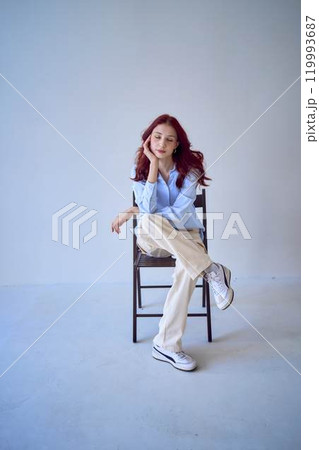portrait of a beautiful teenage girl with red hair sitting on a chair on a white background 119993687