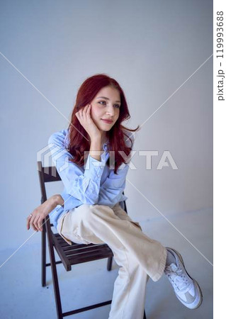 portrait of a beautiful teenage girl with red hair sitting on a chair on a white background 119993688