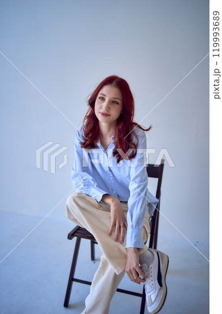 portrait of a beautiful teenage girl with red hair sitting on a chair on a white background portrait of a beautiful teenage girl with red hair sitting on a chair on a white background 119993689