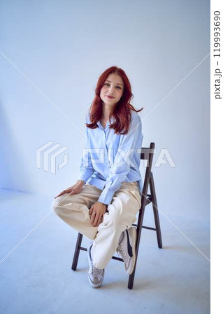 portrait of a beautiful teenage girl with red hair sitting on a chair on a white background 119993690