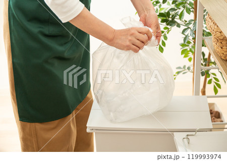 資源ゴミを捨てる緑のエプロンをしたミドル〜シニア女性 119993974