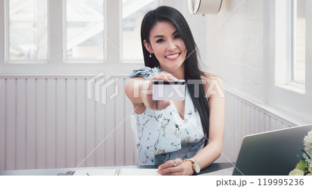 Smiling beautiful Asian woman presenting credit card in hand showing trust and confidence for making payment. Online shopping concept. Smiling beautiful Asian woman presenting credit card in hand showing trust and confidence for making payment. Online shopping concept. 119995236