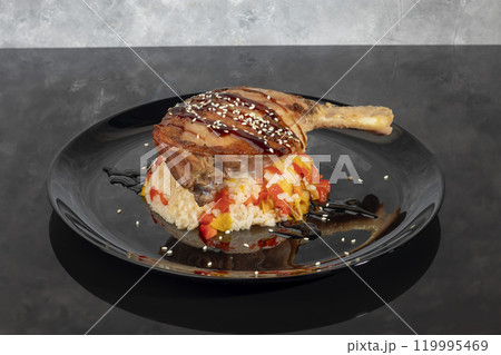 Duck leg in sauce sprinkled with sesame seeds on rice with vegetables. 119995469