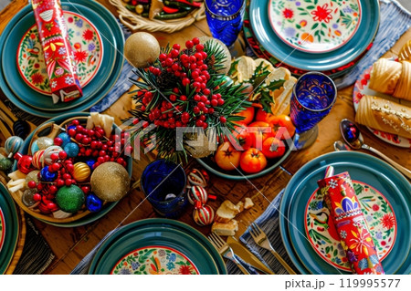 A family Christmas dinner table set with colorful plates, Christmas crackers, and a variety of festive foods is centered around a joyful and vibrant holiday centerpiece 119995577