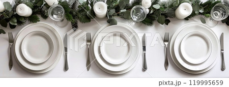 The modern holiday table is elegantly set with white plates and silver cutlery, complemented by minimalistic decor and fresh greenery, offering a clean and stylish Christmas dining experience 119995659
