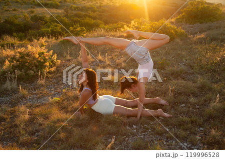 Fly yoga. Women gymnasts practicing in the bright rays of the sunset Fly yoga. Women gymnasts practicing in the bright rays of the sunset 119996528