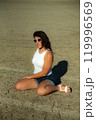 Vertical composition. Portrait young woman in sunglasses sits on dry desert ground 119996569