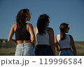 Three young attractive women stand with their backs turned and their heads turned in profile 119996584
