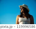 Portrait in profile of young woman in white dress and sunglasses with hat posing against the backdrop of sky 119996586