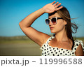 Young woman in white polka dot dress and sunglasses poses against the backdrop of nature. Close-up 119996588