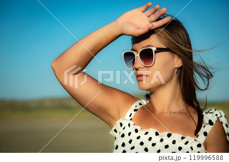 Young woman in white polka dot dress and sunglasses poses against the backdrop of nature. Close-up 119996588
