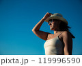 Portrait Young woman in white dress and sunglasses with hat posing against the backdrop of sky. Close-up 119996590