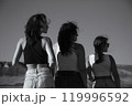 Black and white photo. Three young attractive women stand with their backs turned and their heads turned in profile 119996592