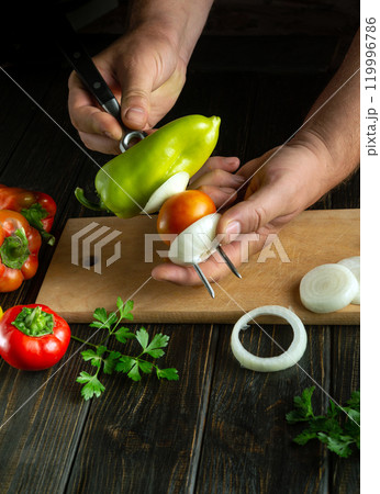A hand skillfully stacks colorful vegetables, including bell peppers and tomatoes, onto a skewer, set against a rustic wooden table filled with fresh ingredients A hand skillfully stacks colorful vegetables, including bell peppers and tomatoes, onto a skewer, set against a rustic wooden table filled with fresh ingredients 119996786