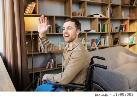 Man on wheelchair in room looking through window and smiling. Side view of young disabled patient in wheelchair looking out window Man on wheelchair in room looking through window and smiling. Side view of young disabled patient in wheelchair looking out window 119998092