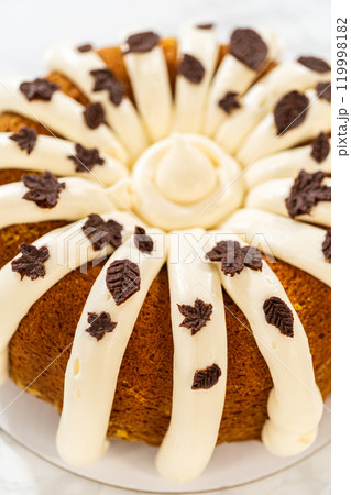Icing the pumpkin bundt cake with cream cheese frosting and decorating it with chocolate leaves. 119998182