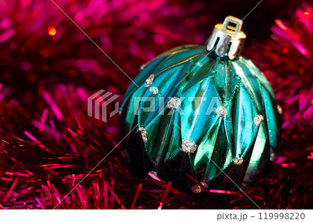 Close-up of green Christmass ball on the red tinsel garland. Close-up of green Christmass ball on the red tinsel garland. 119998220