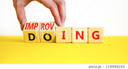 Doing or improving symbol. Businessman turns wooden cubes and changes the word Doing to Improving. Beautiful yellow table white background. Educational business doing or improving concept. Copy space 119998283