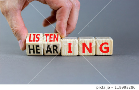 Listening or hearing symbol. Businessman turns wooden cubes and changes a concept word Listening to Hearing. Beautiful grey background. Copy space. Business educational listening or hearing concept. Listening or hearing symbol. Businessman turns wooden cubes and changes a concept word Listening to Hearing. Beautiful grey background. Copy space. Business educational listening or hearing concept. 119998286