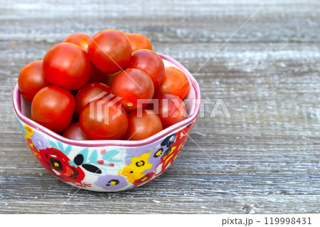 Red cherry tomatoes in a bowl with floral pattern. 119998431