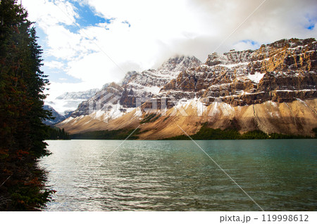 Mountains covered with snow above the lake with turquoise waters in a cold autumn day with cloudy sky. Bow lake, Banff national park, Canada. 119998612