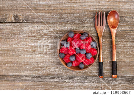 Mix of blueberries and raspberries in a plate with wooden fork and spoon. 119998667