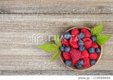 Plate with raspberries and blueberries with leaves on the wooden rustic table. 119998668