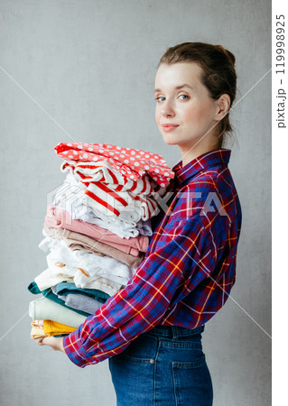 Housewife girl holds stack of clean clothes in hands after washing, drying.  119998925