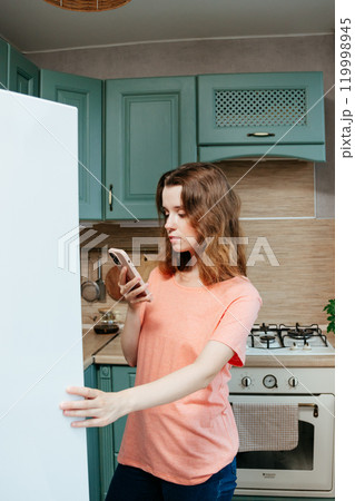 young woman looks into refrigerator in kitchen, orders food from delivery service, restaurant. 119998945