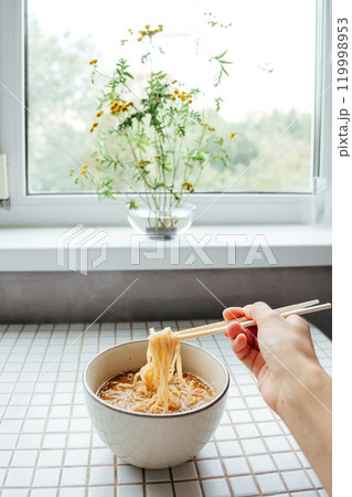 Asian fast food, person using chopsticks to eat instant ramen, noodle soup from bowl at home 119998953