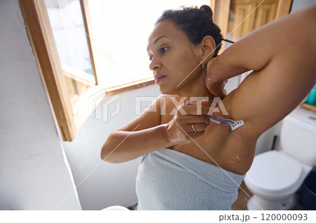 Woman shaving underarm with razor in a bright bathroom Woman shaving underarm with razor in a bright bathroom 120000093