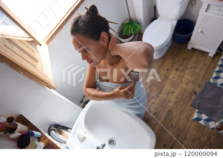 Woman shaving armpit in bathroom wrapped in towel 120000094