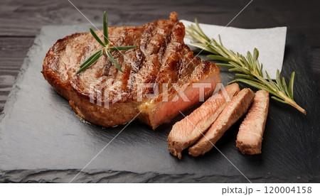 Medium rare juicy steak, parchment paper and rosemary on a slate plate 120004158