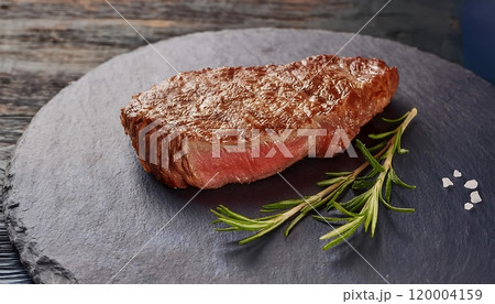 Medium rare juicy steak, parchment paper and rosemary on a slate plate 120004159