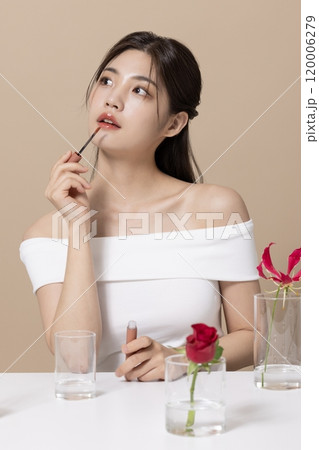 a woman in her 20s holding cosmetics in front of a table decorated with flowers a woman in her 20s holding cosmetics in front of a table decorated with flowers 120006279