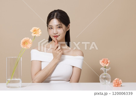 a woman in her 20s holding cosmetics in front of a table decorated with flowers 120006339