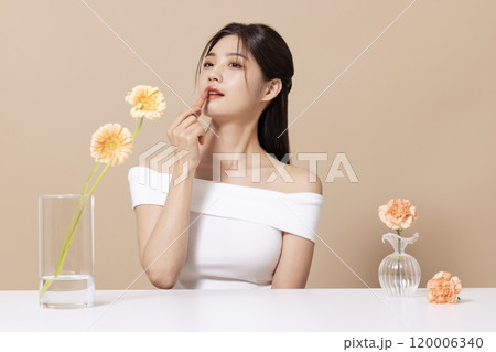 a woman in her 20s holding cosmetics in front of a table decorated with flowers a woman in her 20s holding cosmetics in front of a table decorated with flowers 120006340