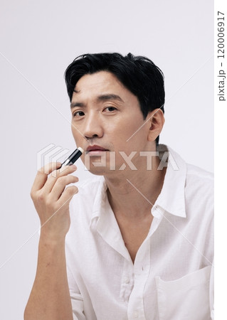 A pose of a middleaged man applying lip balm to his lips A pose of a middleaged man applying lip balm to his lips 120006917