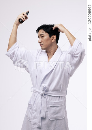 A middleaged man holding a spray bottle and spraying mist on his head 120006966