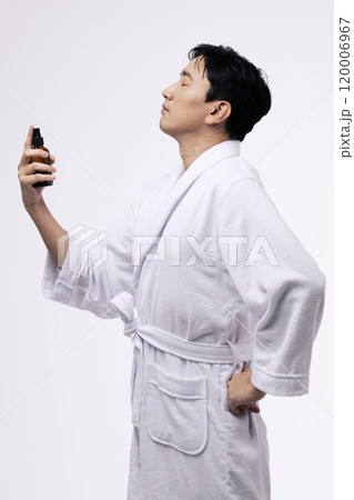 Middleaged man holding a spray bottle and spraying mist on his face 120006967