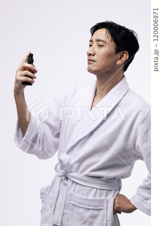 Middleaged man holding a spray bottle and spraying mist on his face 120006971