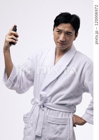 Middleaged man holding a spray bottle and spraying mist on his face Middleaged man holding a spray bottle and spraying mist on his face 120006972