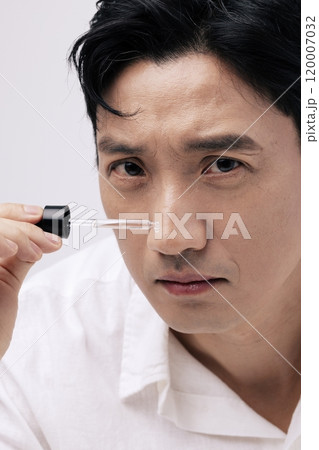 Closeup of a middleaged man holding a dropper with an ampoule and looking straight ahead. 120007032