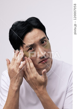 A middleaged man attaching an eye patch to his eye area with his finger. 120007058