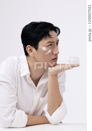 A middleaged man holding a can of cream in his palm with a frowning expression 120007081
