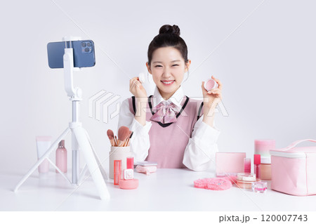A teenage woman in school uniform laying out various cosmetics and filming a video with her smartphone 120007743