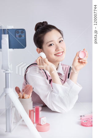 A teenage woman in school uniform laying out various cosmetics and filming a video with her smartphone A teenage woman in school uniform laying out various cosmetics and filming a video with her smartphone 120007744