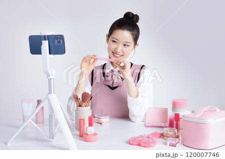 A teenage woman in school uniform laying out various cosmetics and filming a video with her smartphone 120007746